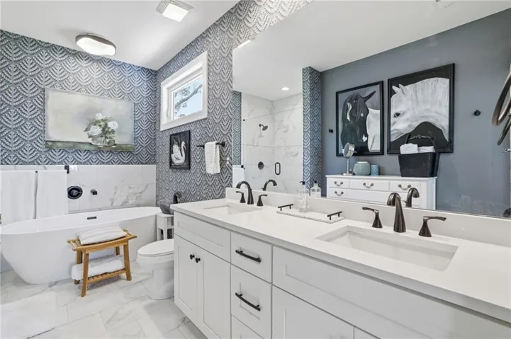 Bathroom featuring a freestanding soaking tub, dual vanity with undermount sinks, separate walk-in shower with clear glass enclosure, and white marble-look tile flooring