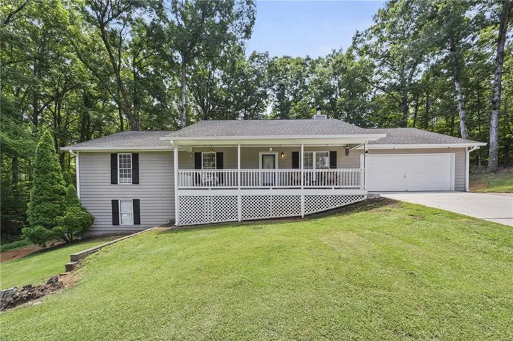 Ranch-style residence featuring a covered front porch with white railings and lattice work, an attached two-car garage, light-colored siding, and a sloped front yard with mature trees