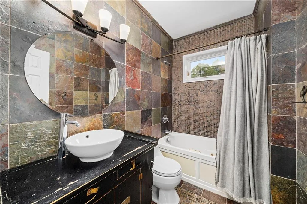 Bathroom with tile walls, shower / bathtub combination with curtain, and vanity