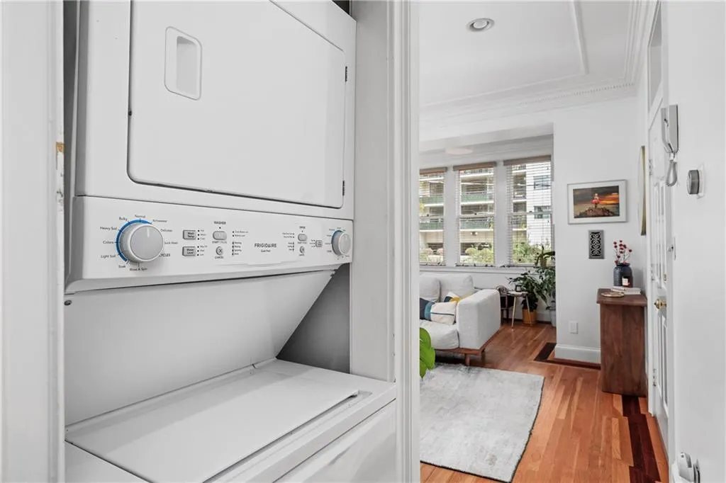 Washroom with light wood-style flooring, crown molding, and stacked washing machine and dryer