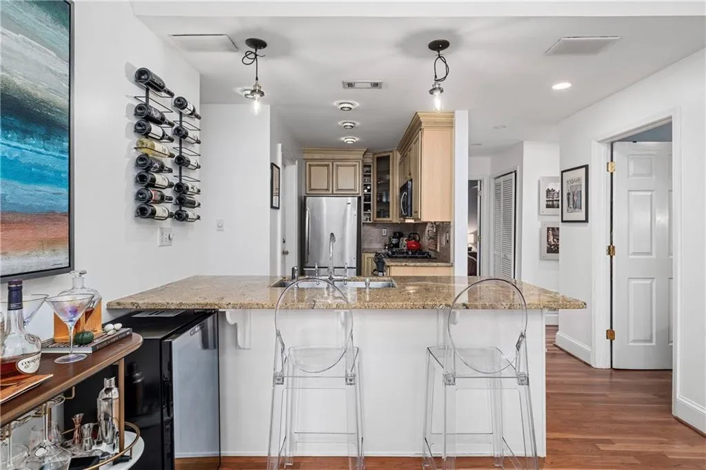 Kitchen featuring a breakfast bar, light stone countertops, dark wood-type flooring, stainless steel appliances, and pendant lighting