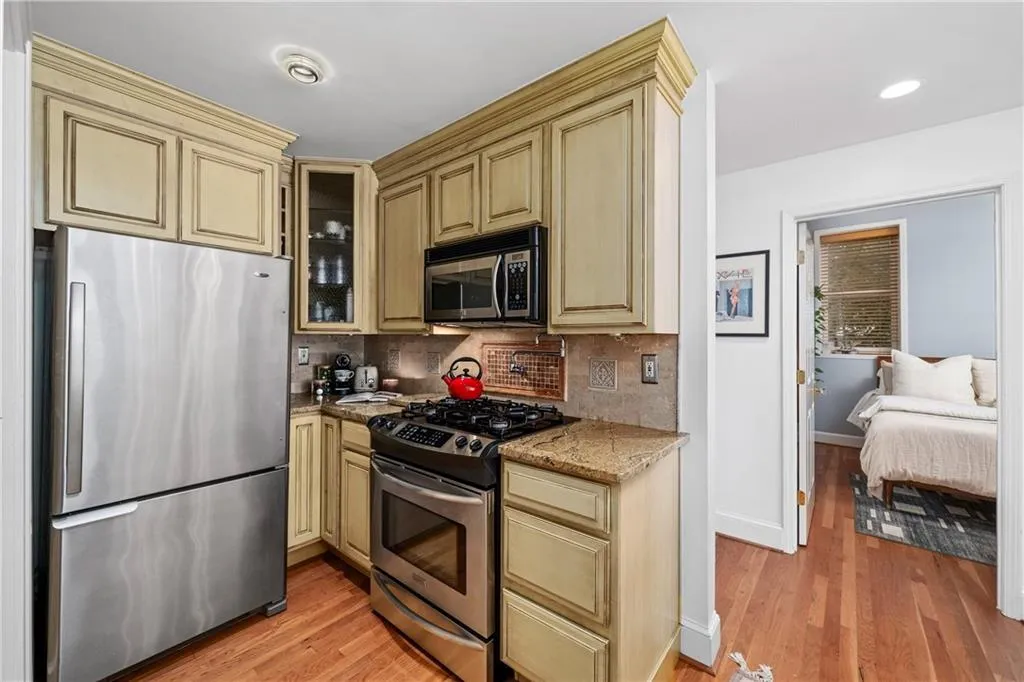 Kitchen featuring stainless steel appliances, decorative backsplash, light stone countertops, light wood-type flooring, and glass insert cabinets