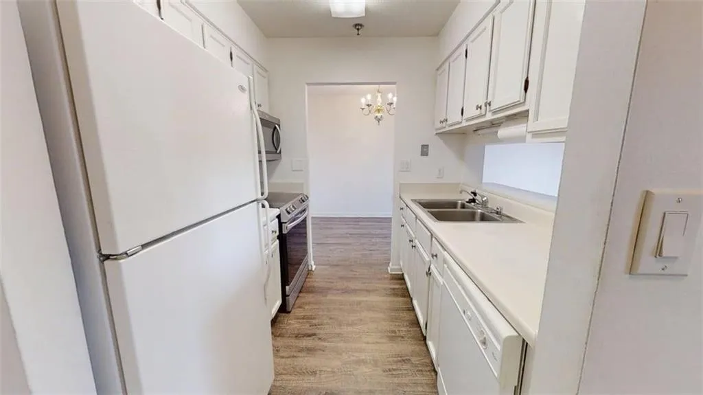 Kitchen with appliances with stainless steel finishes, white cabinetry, a chandelier, light countertops, and light wood-type flooring