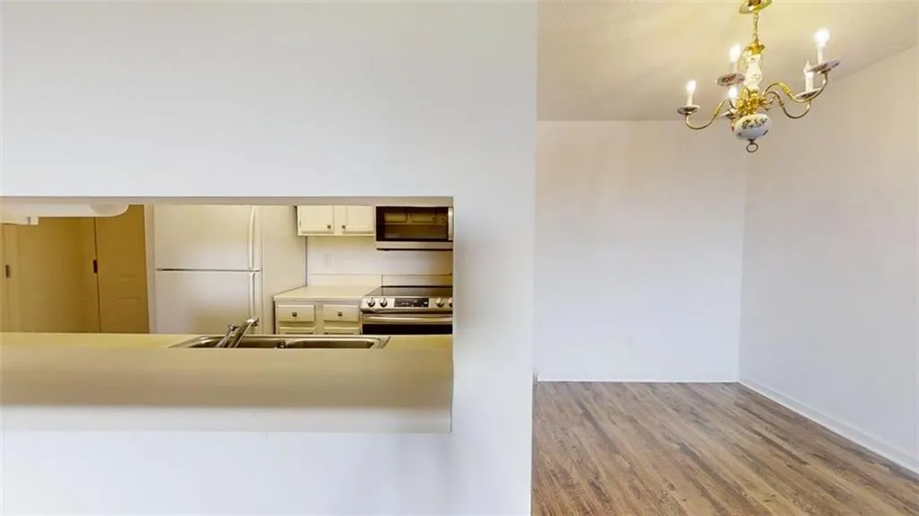 Kitchen featuring light countertops, appliances with stainless steel finishes, wood finished floors, decorative light fixtures, and a chandelier