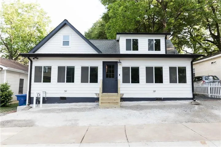 White siding exterior with black trim, a dark entry door, multiple windows, and a gravel front area