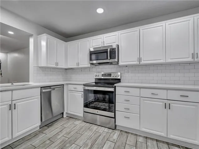 White cabinetry with stainless steel appliances, light countertops, subway tile backsplash, and wood-finish flooring
