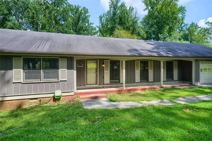 Single-story residence featuring a covered front porch, attached garage, and a mature tree backdrop