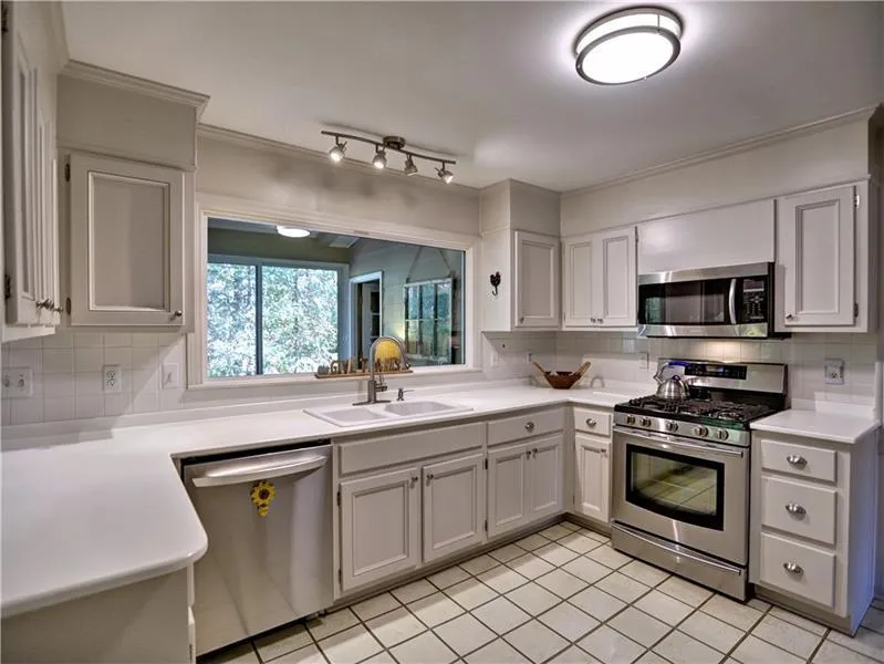 Kitchen with white cabinets, appliances with stainless steel finishes, tasteful backsplash, and sink