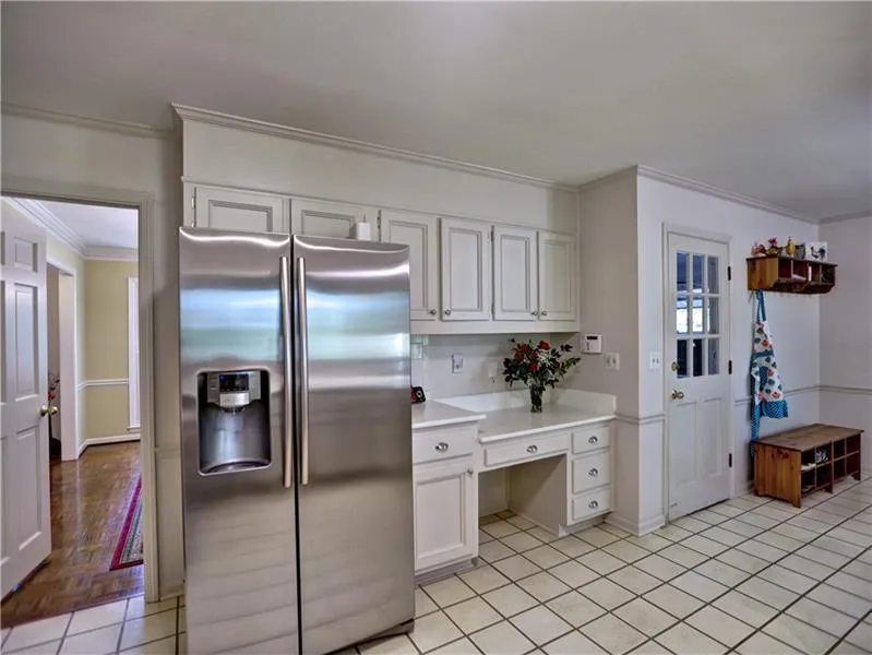 Kitchen with stainless steel refrigerator with ice dispenser, white cabinetry, ornamental molding, and light tile patterned flooring