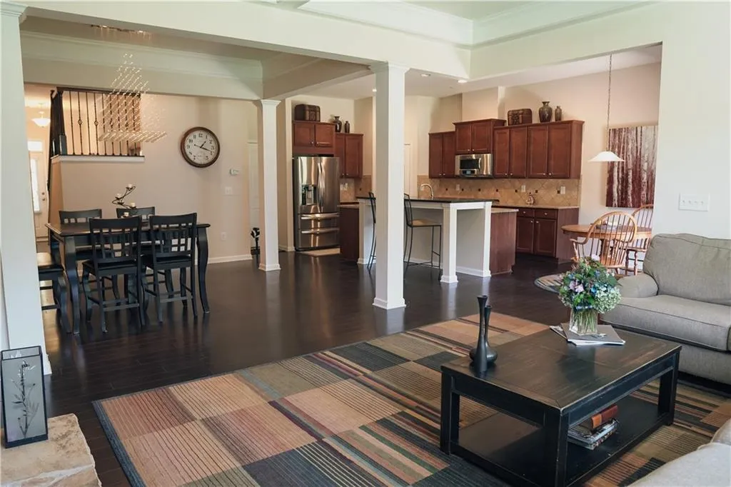 Living room with decorative columns, crown molding, a raised ceiling, and dark wood-type flooring