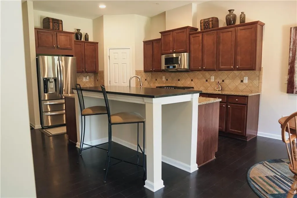 Kitchen with appliances with stainless steel finishes, dark hardwood / wood-style flooring, a kitchen breakfast bar, and backsplash