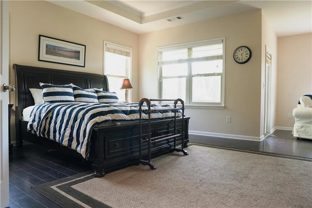 Bedroom featuring dark wood-type flooring, multiple windows, ornamental molding, and a raised ceiling