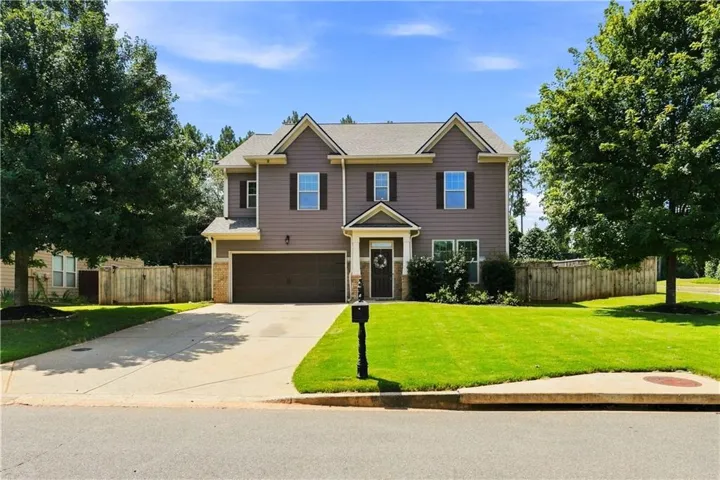 Two-story residence featuring a two-car garage, front-facing gables, and a mature treed lot