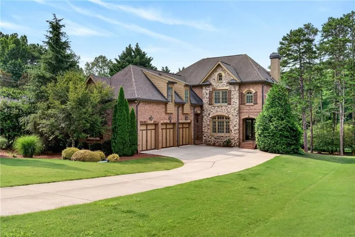Brick and stone facade residence featuring a multi-car garage, mature trees, and a paved driveway