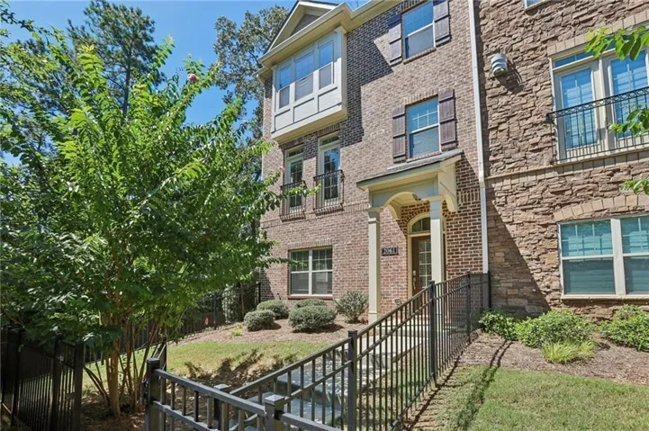 Brick and stone facade townhome featuring a front entry porch with columns, decorative window shutters, and an upper-level bay window