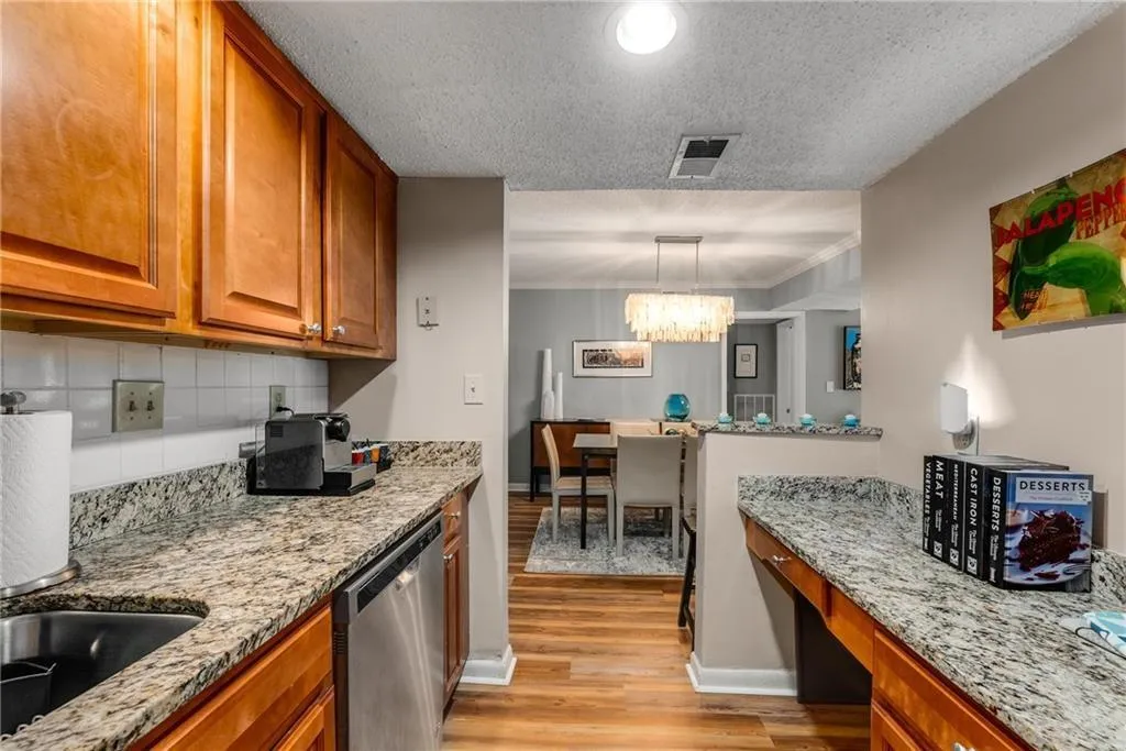 Kitchen with wood finish cabinetry, light stone countertops, stainless steel dishwasher, a textured ceiling, and light wood-style flooring