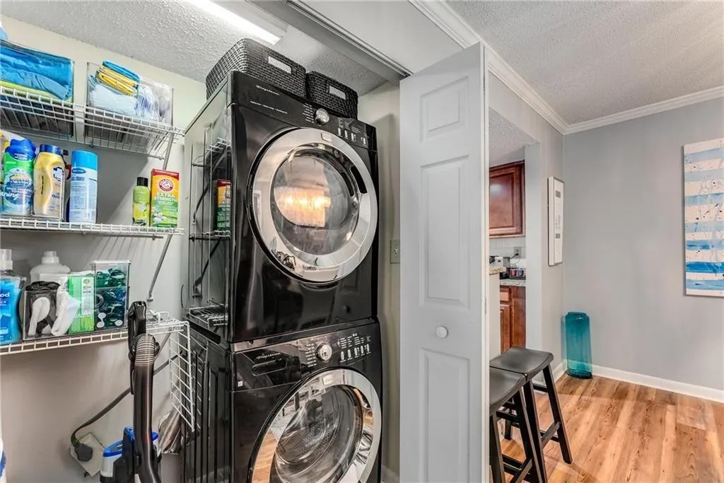 Laundry area with a textured ceiling, light wood finished floors, stacked washer / dryer, and crown molding
