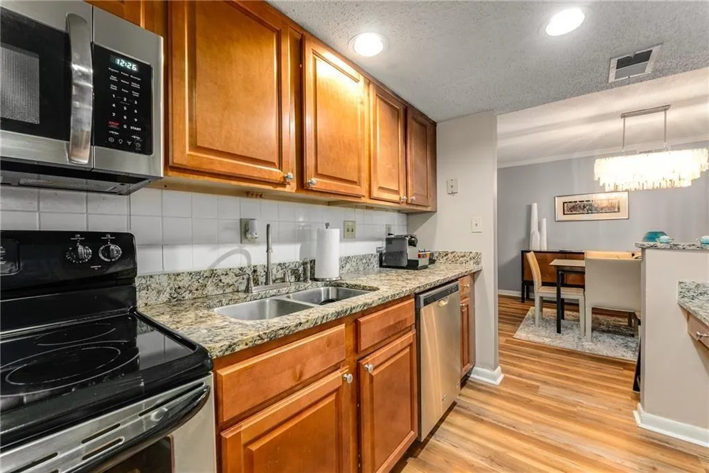 Kitchen with stainless steel appliances, wood finish cabinetry, light stone counters, light wood-type flooring, and a textured ceiling
