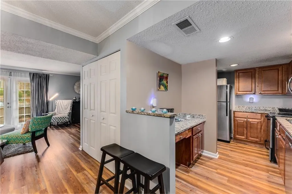 Kitchen featuring a textured ceiling, light wood-style floors, wood finish cabinetry, stainless steel appliances, and light stone counters