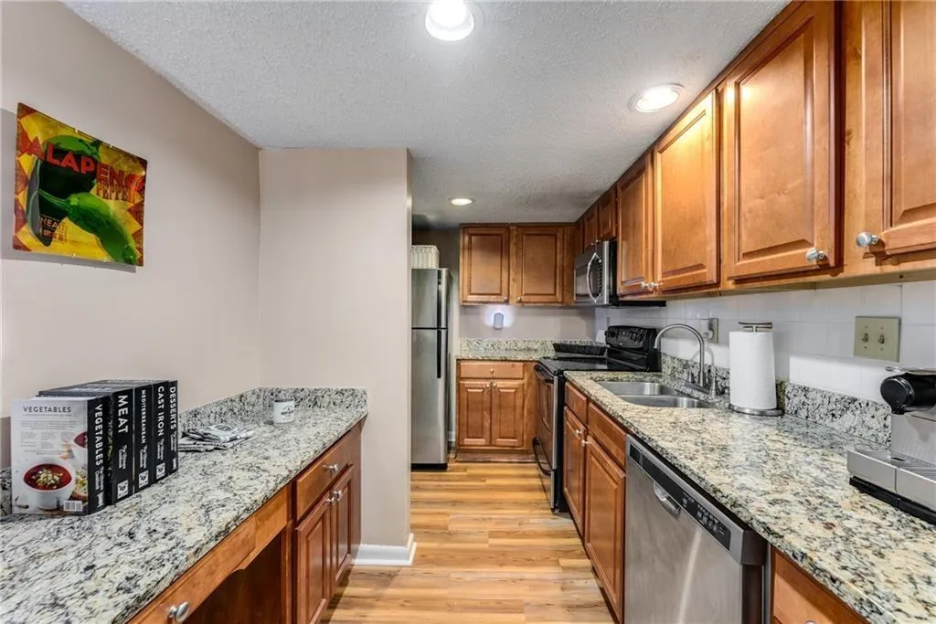 Kitchen featuring wood finish cabinetry, recessed lighting, stainless steel appliances, light wood-type flooring, and light stone counters
