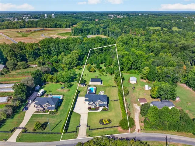 Expansive property featuring a residence with a large driveway, a swimming pool, a detached garage, and mature trees