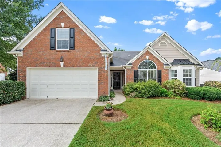 Brick exterior with siding accents, arched transom window, bay window, two-car garage, and established landscaping
