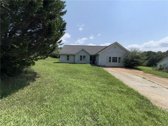Charming single-story residence set on expansive grounds featuring a manicured lawn, mature tree line, and a long driveway approach