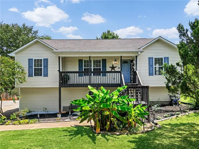 Exterior featuring light-toned horizontal siding, a covered porch with black railings, a blue front door, and a multi-level deck with stairs