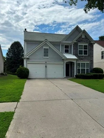 Two-story residential structure featuring a prominent stone facade accent and siding, a dual-door garage, and a concrete driveway