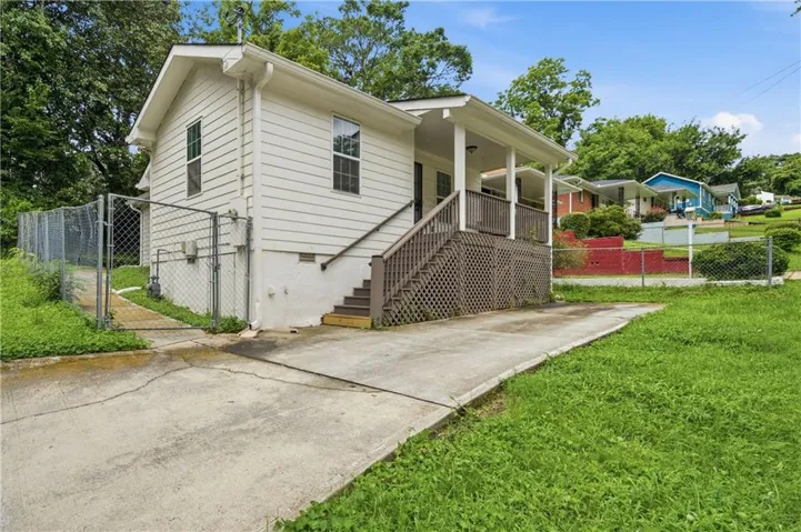 White horizontal siding exterior with a front porch featuring a lattice skirt, a concrete driveway, and a chain-link fence