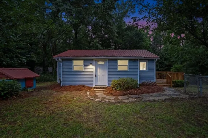 Light blue siding exterior with a red metal roof, front entry with transom window, stone pathway, and an exterior deck