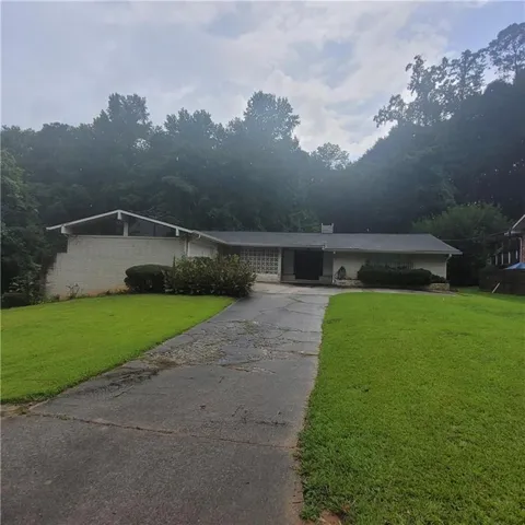 Brick exterior with a peaked roofline, front lawn, and mature trees in the background