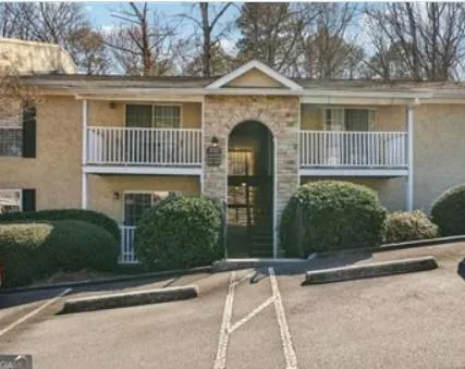 Two-story building exterior featuring a stone facade archway, stucco siding, and white balcony railings