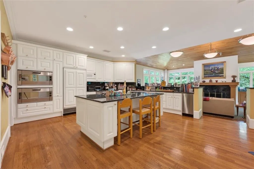 Spacious chef's kitchen featuring white cabinetry with paneled doors, a large center island with seating for multiple, stainless steel appliances, black countertops, and recessed lighting throughout