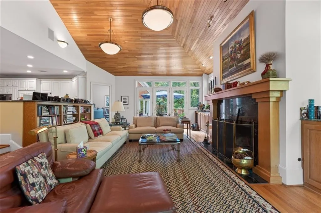 Spacious living room featuring warm wood-finish ceiling with recessed lighting, a wood-burning fireplace with dark surround, and hardwood flooring throughout