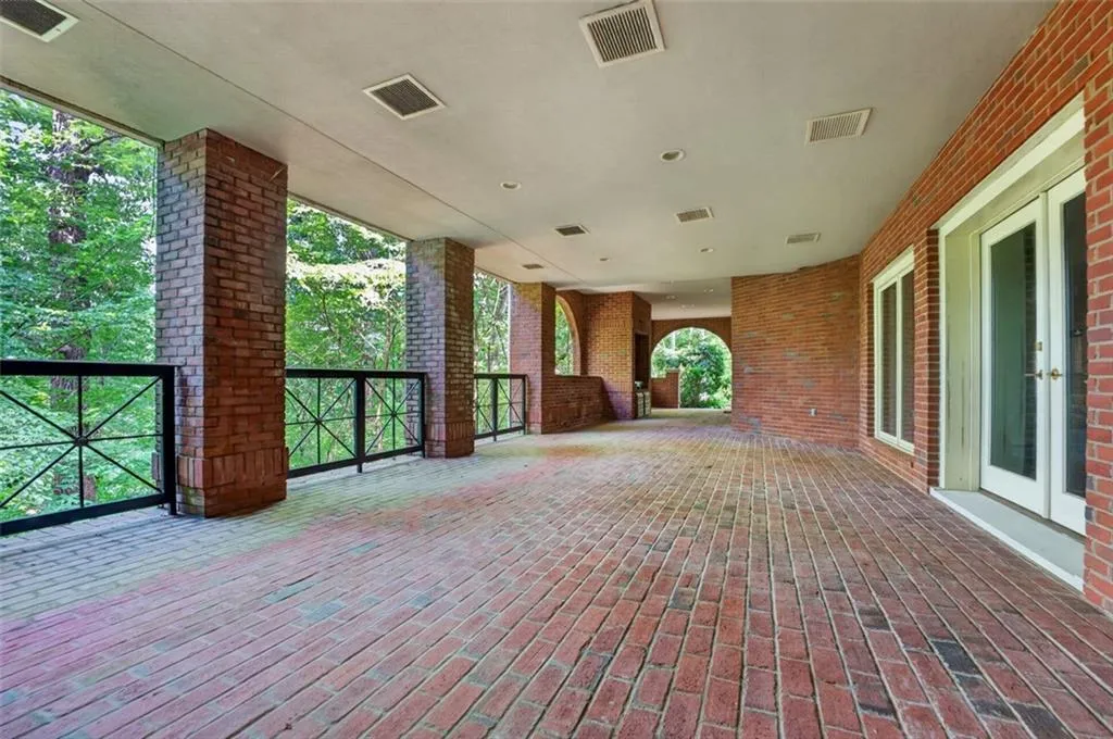 Expansive covered patio featuring a brick paver floor, brick columns, and wrought iron railings