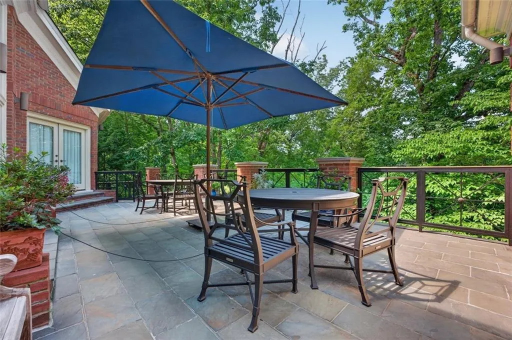 Spacious outdoor patio with natural stone flooring, a brick exterior wall, and iron railings