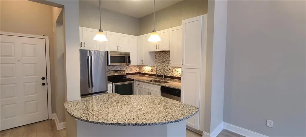 Kitchen with light stone counters, a sink, tasteful backsplash, appliances with stainless steel finishes, and white cabinetry