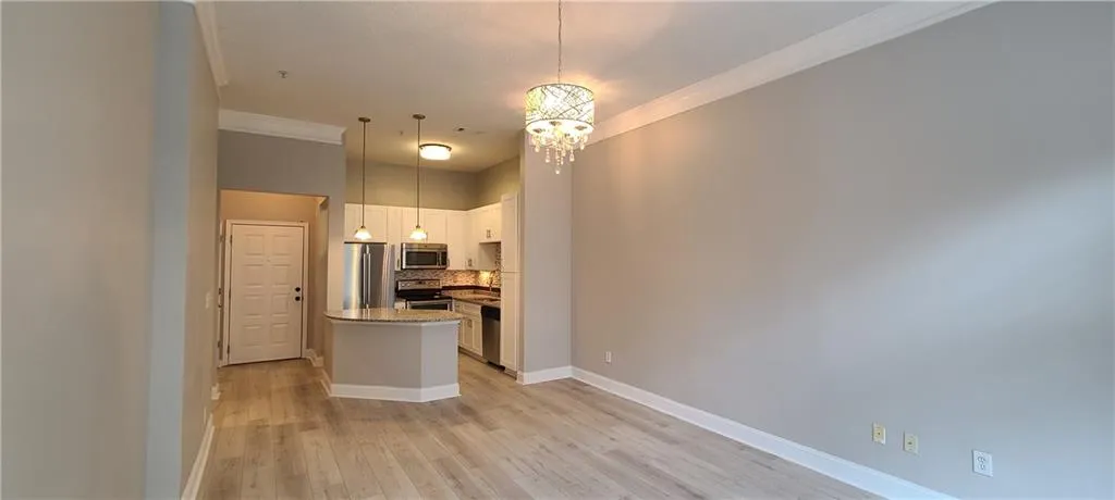 Kitchen with backsplash, ornamental molding, light wood-type flooring, a chandelier, and appliances with stainless steel finishes