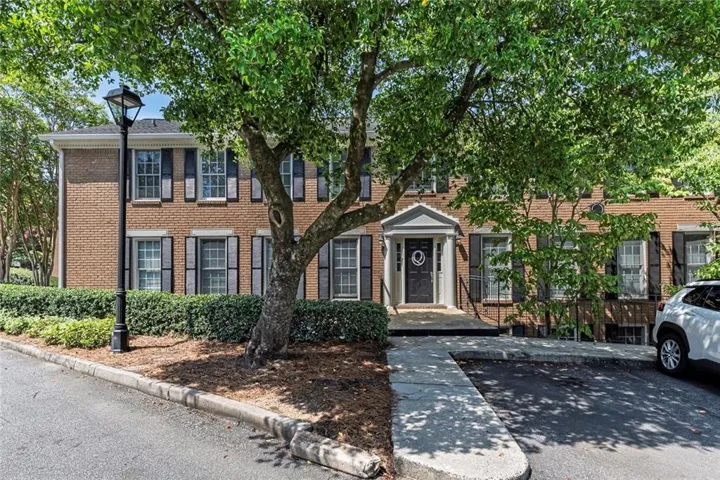 Brick Colonial residence featuring a welcoming front entrance with a covered portico, multi-pane windows, and mature landscaping with established trees and manicured shrub borders