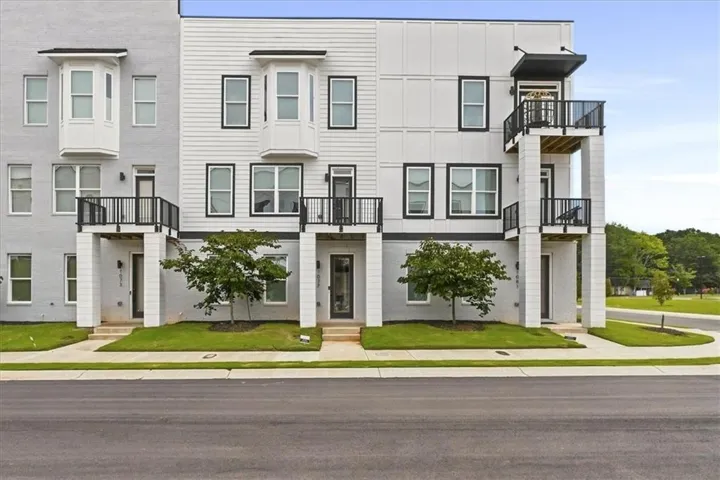 Modern farmhouse exterior featuring clean horizontal siding, multiple multi-pane windows with dark trim, covered front porches with black railings, and tiered architectural design