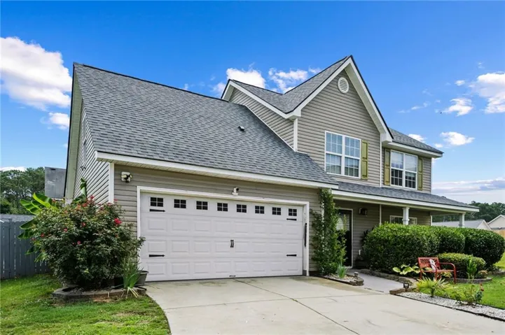 Two-story residence featuring light gray siding, a two-car garage with panel detailing, and a covered front porch