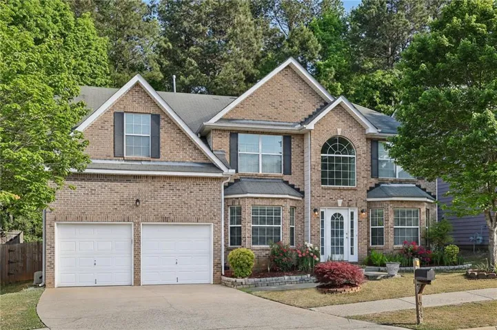 Brick facade with gabled roofline, arched front window, two-car garage, and mature landscaping