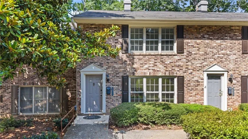 Brick facade residence featuring multiple pane windows with dark shutters, a light-colored entry door with a decorative surround, and established front landscaping