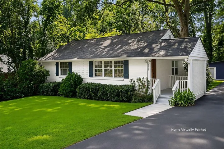 White brick exterior, dark shingle roof, established landscaping, covered front entry, paved driveway