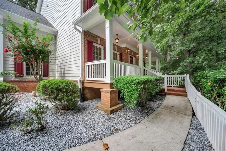 White siding exterior with red brick accents, an inviting front porch with white railings, and a concrete pathway