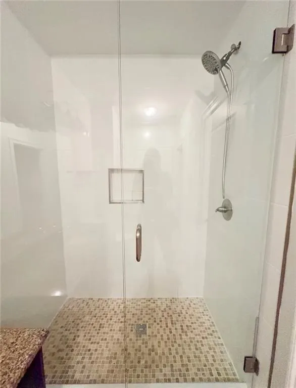 Walk-in shower with clear glass enclosure, mosaic tile floor, built-in shower niche, and brushed nickel fixtures