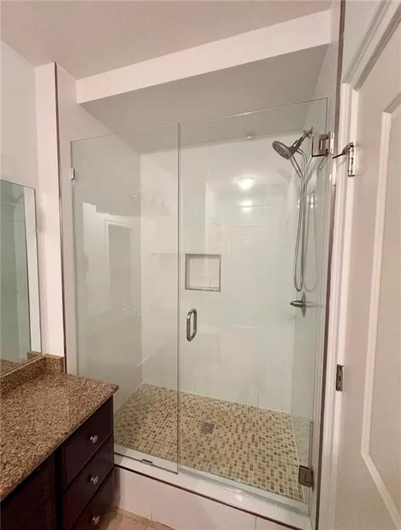 Walk-in shower with clear glass enclosure, mosaic tile flooring, built-in shower niche, and a rain showerhead
