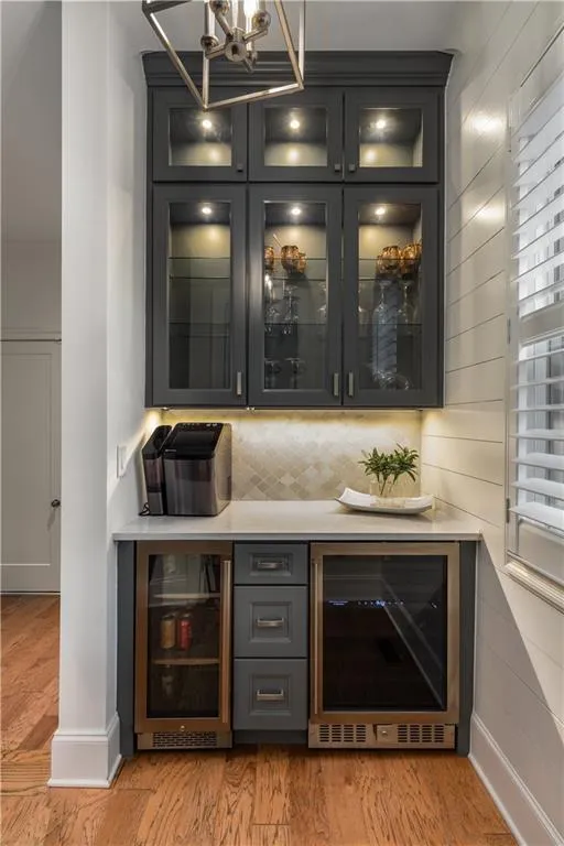 Bar featuring wine cooler, a notable chandelier, decorative backsplash, and light wood-type flooring