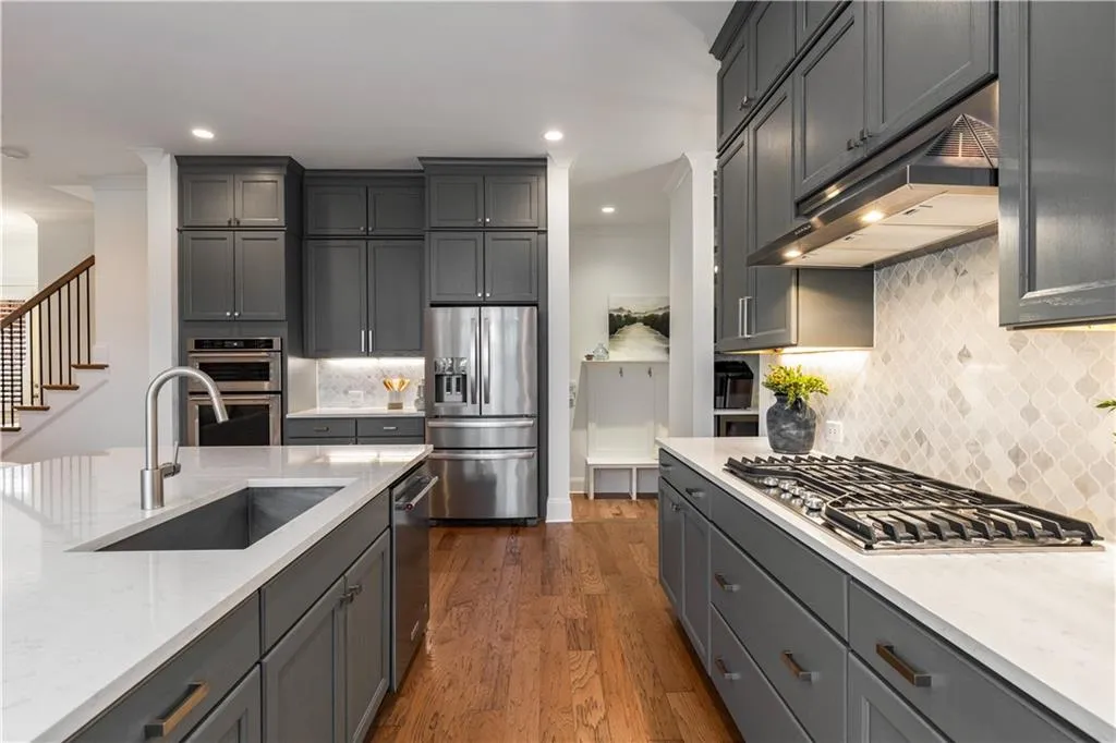 Kitchen with appliances with stainless steel finishes, sink, gray cabinetry, dark hardwood / wood-style flooring, and light stone countertops